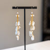 Pair of gold and pearl drop earrings on a black stand against a neutral background