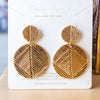 Gold geometric earrings on a branded card with a blurred background