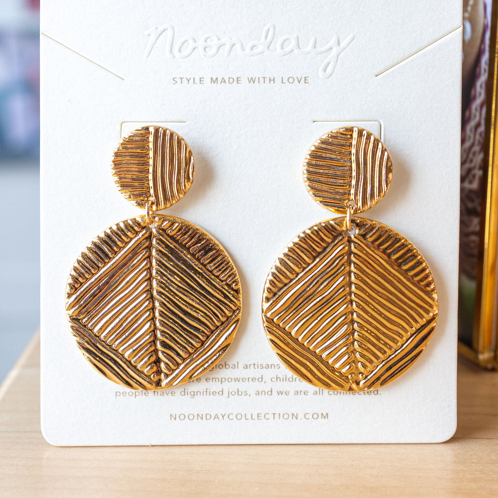 Gold geometric earrings on a branded card with a blurred background