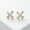 Pair of white X-shaped earrings with gold accents on a light gray background