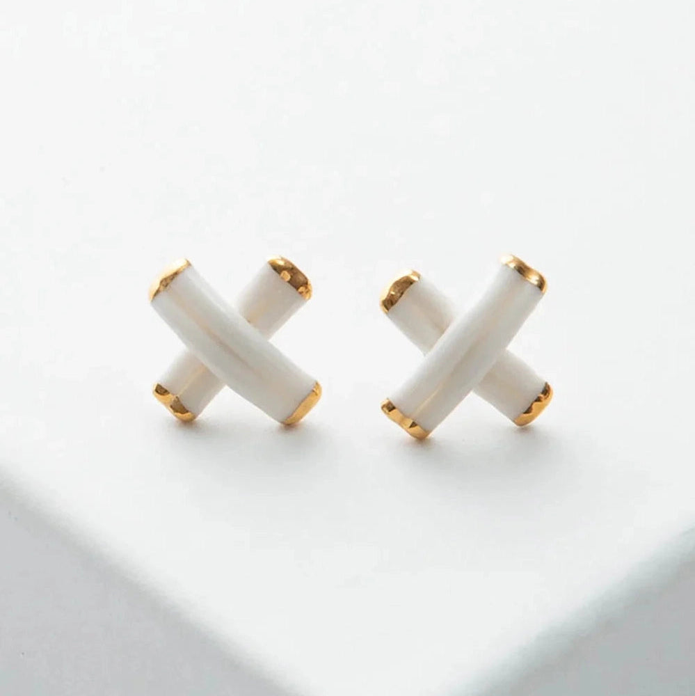 Pair of white X-shaped earrings with gold accents on a light gray background