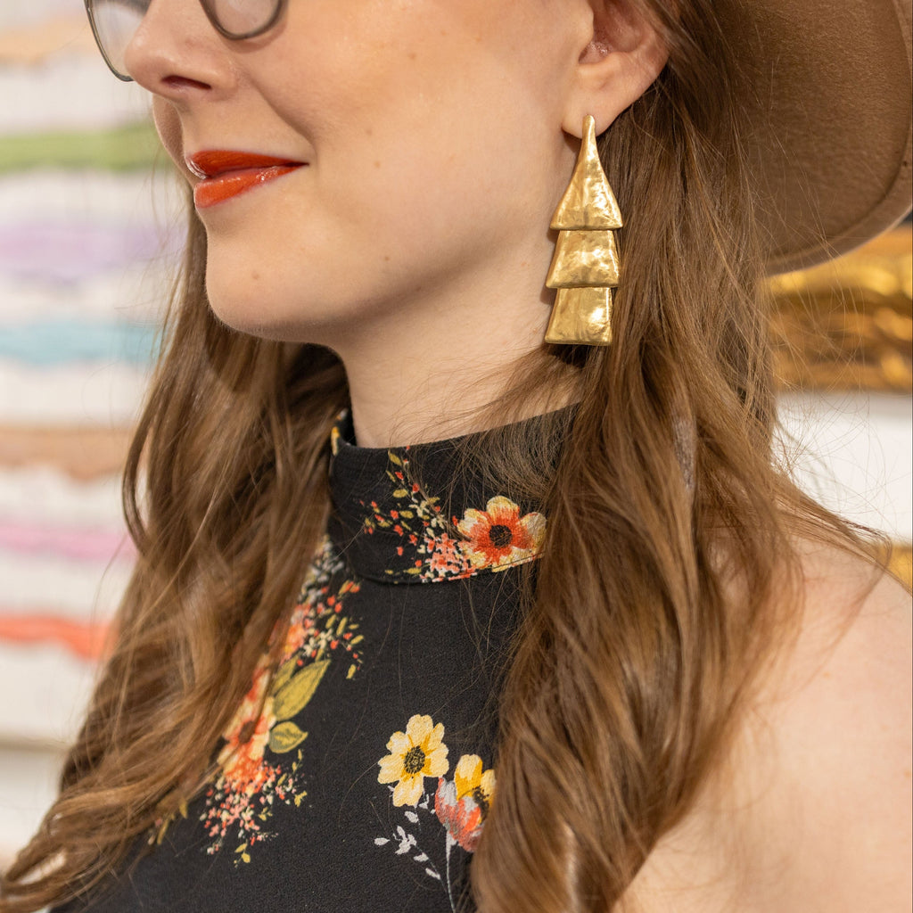 Woman wearing a floral dress and gold earrings with a blurred background of art supplies.
