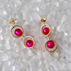Gold earrings with pink gemstones on a textured white surface