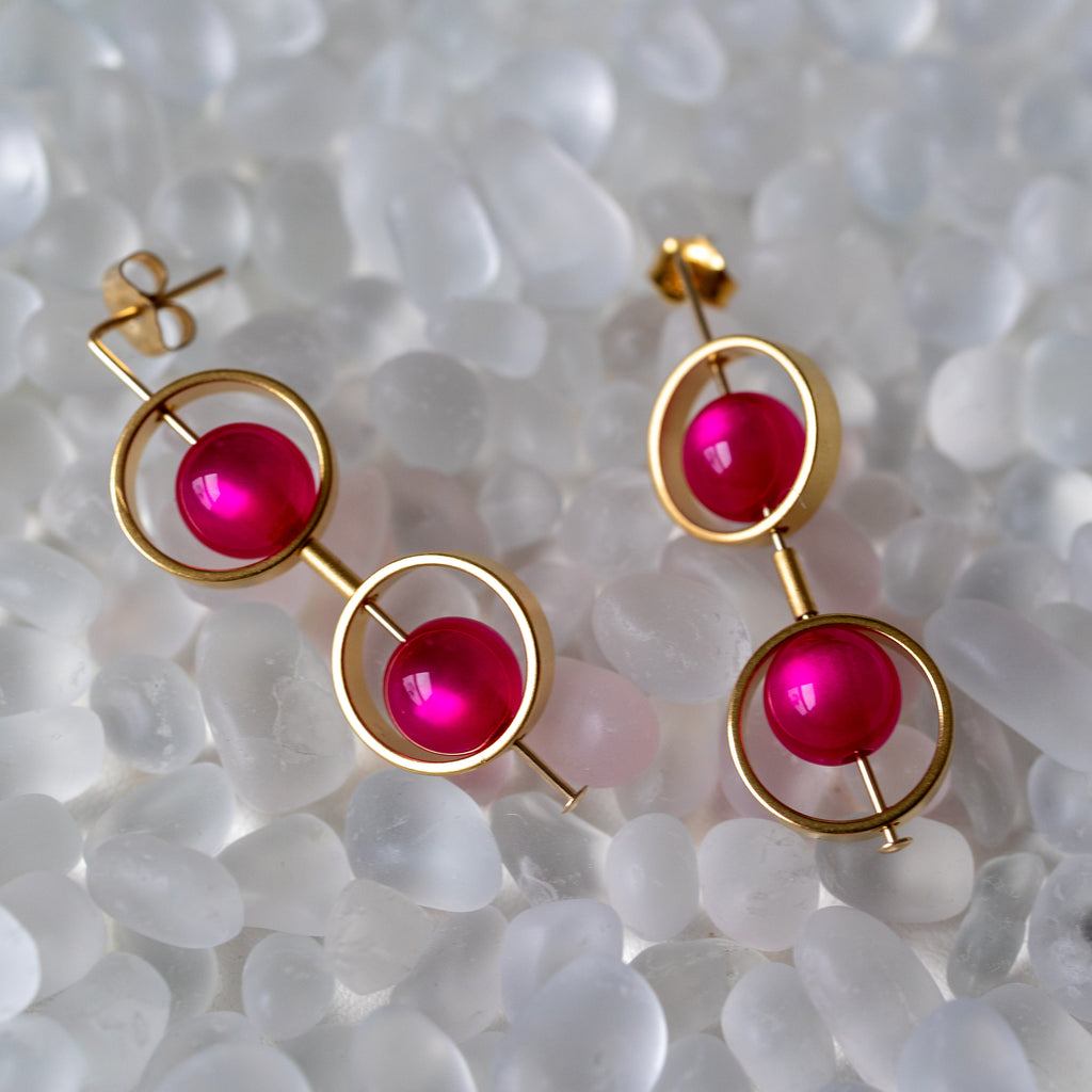 Gold earrings with pink gemstones on a textured white surface