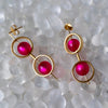 Gold earrings with pink gemstones on a textured white surface