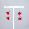 Gold earrings with pink spherical beads on a white stand against a light gray background