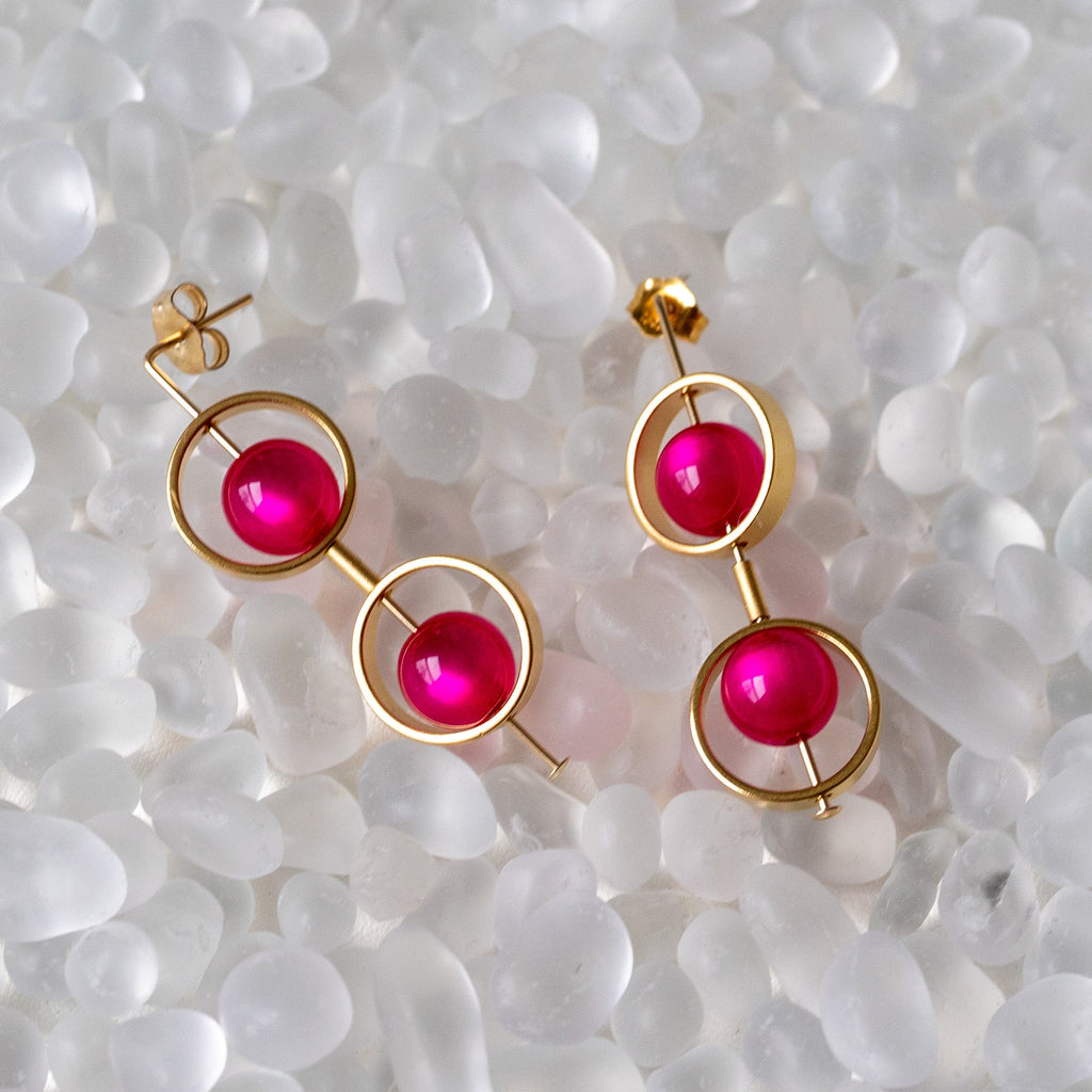 Gold earrings with pink gemstones on a textured white surface