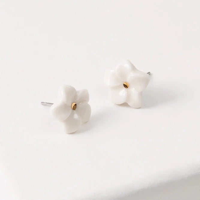 A pair of small white flower stud earrings with gold centers, resting on a clean white surface.
