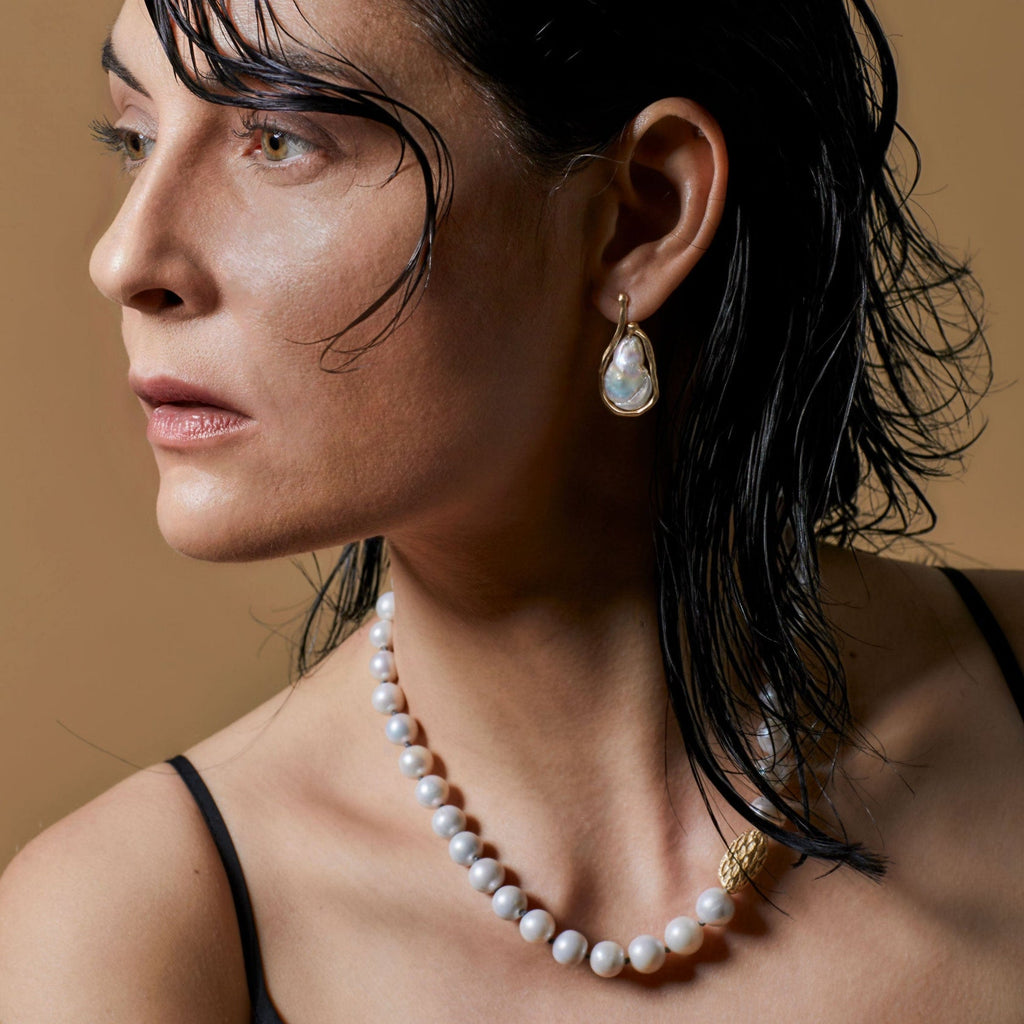 Woman wearing a pearl necklace and gold earrings against a beige background
