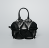 A black structured handbag with a sculptural, layered petal-like design, dual top handles, and small silver-tone studs, photographed on a light gray studio background.