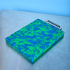 Green and blue camouflage-patterned cutting board with a handle on a light gray surface.
