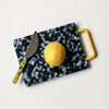 Small black/white cutting board with yellow handle and yellow lemon