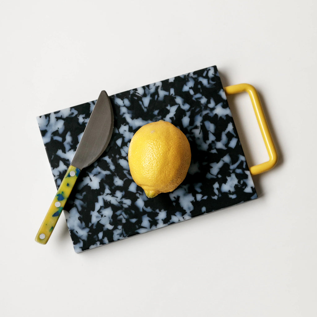 Small black/white cutting board with yellow handle and yellow lemon
