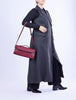 Person wearing a long dark gray coat holding a red handbag on a white background