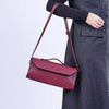 Person wearing a long dark gray coat holding a red handbag on a white background