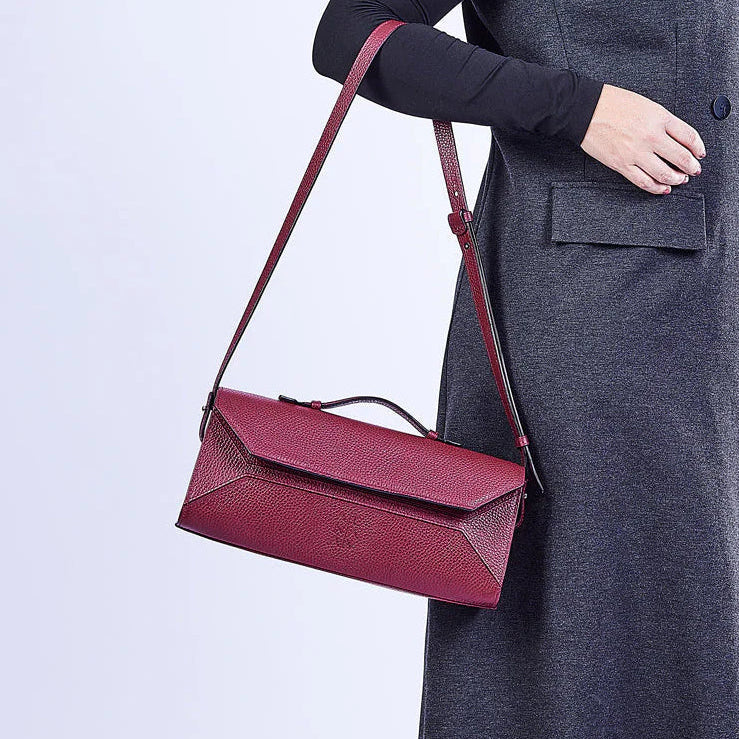 Person wearing a long dark gray coat holding a red handbag on a white background