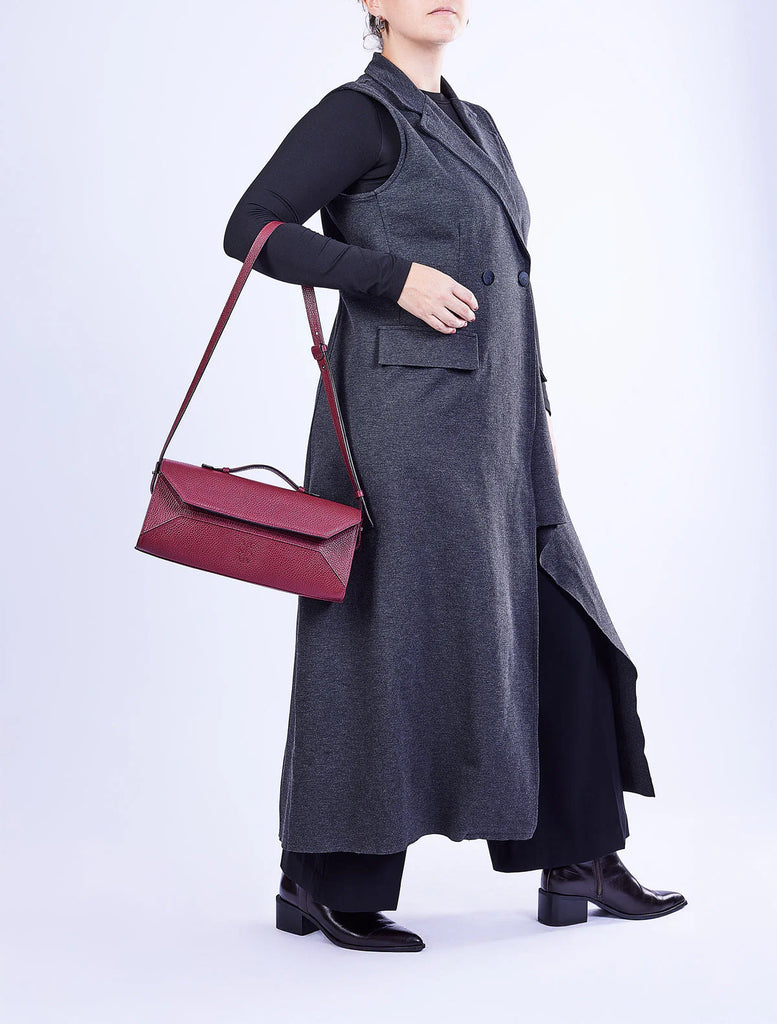 Person wearing a long dark gray coat holding a red handbag on a white background