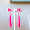 Pink earrings on a white stand with a light blue wall in the background