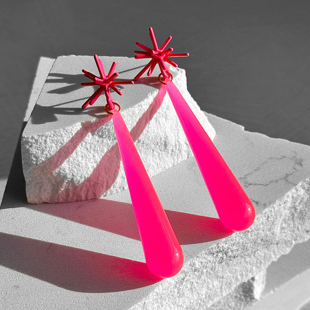Pink earrings with star-shaped tops on a textured surface