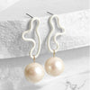 Pearl earrings with white curved hooks on a light gray background