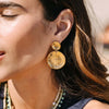 Close-up of a woman wearing gold leaf earrings with layered necklaces.