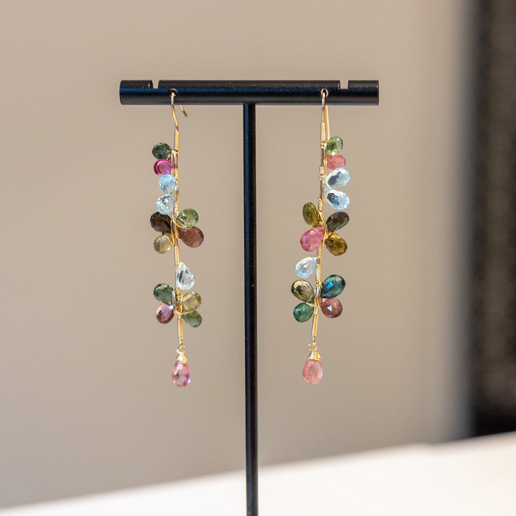 Multicolored beaded earrings on a black display stand against a neutral background