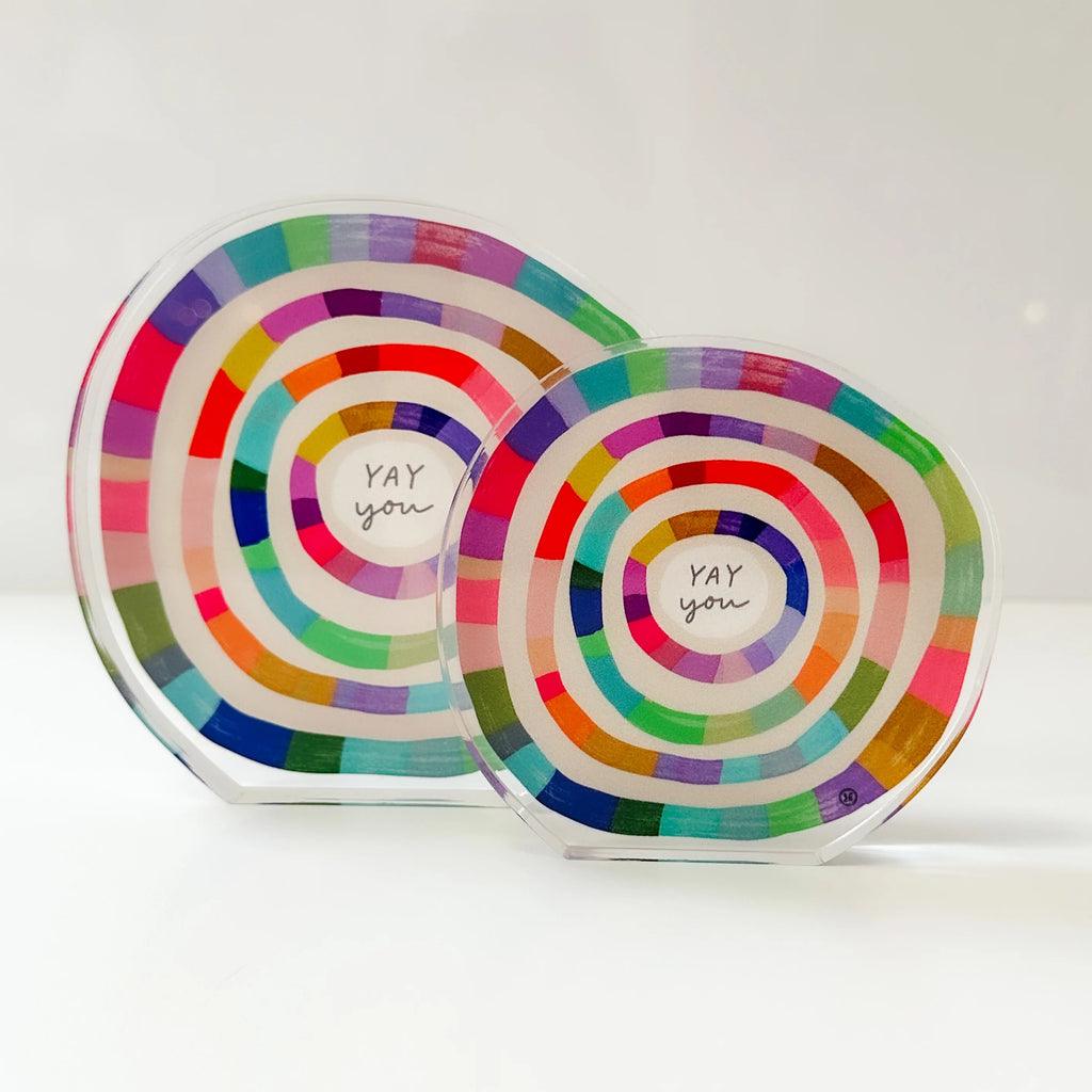 Two clear acrylic round plaques with colorful concentric rainbow stripes and the words 'YAY you' written in the center, displayed on a white surface against a white background.
