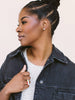 A woman with braided hair in a bun wearing a dark denim jacket over a white knit top, shown in profile against a plain light background.