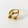 A gold-colored metal ring with two polished spherical beads at the ends, photographed on a clean white background.