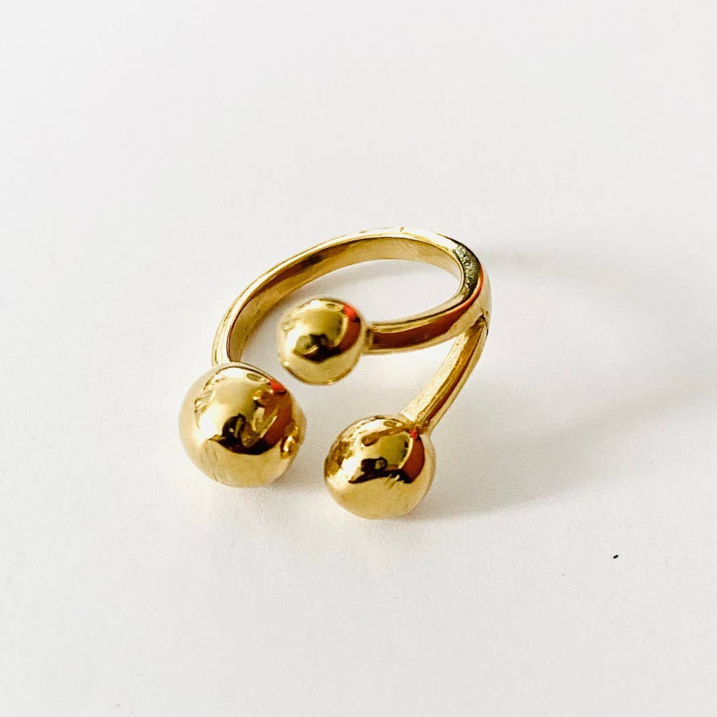 A gold-colored metal ring with two polished spherical beads at the ends, photographed on a clean white background.