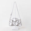 A white shoulder bag with a sculptural, layered petal-like design outlined in black, displayed on a white stand against a clean white background.