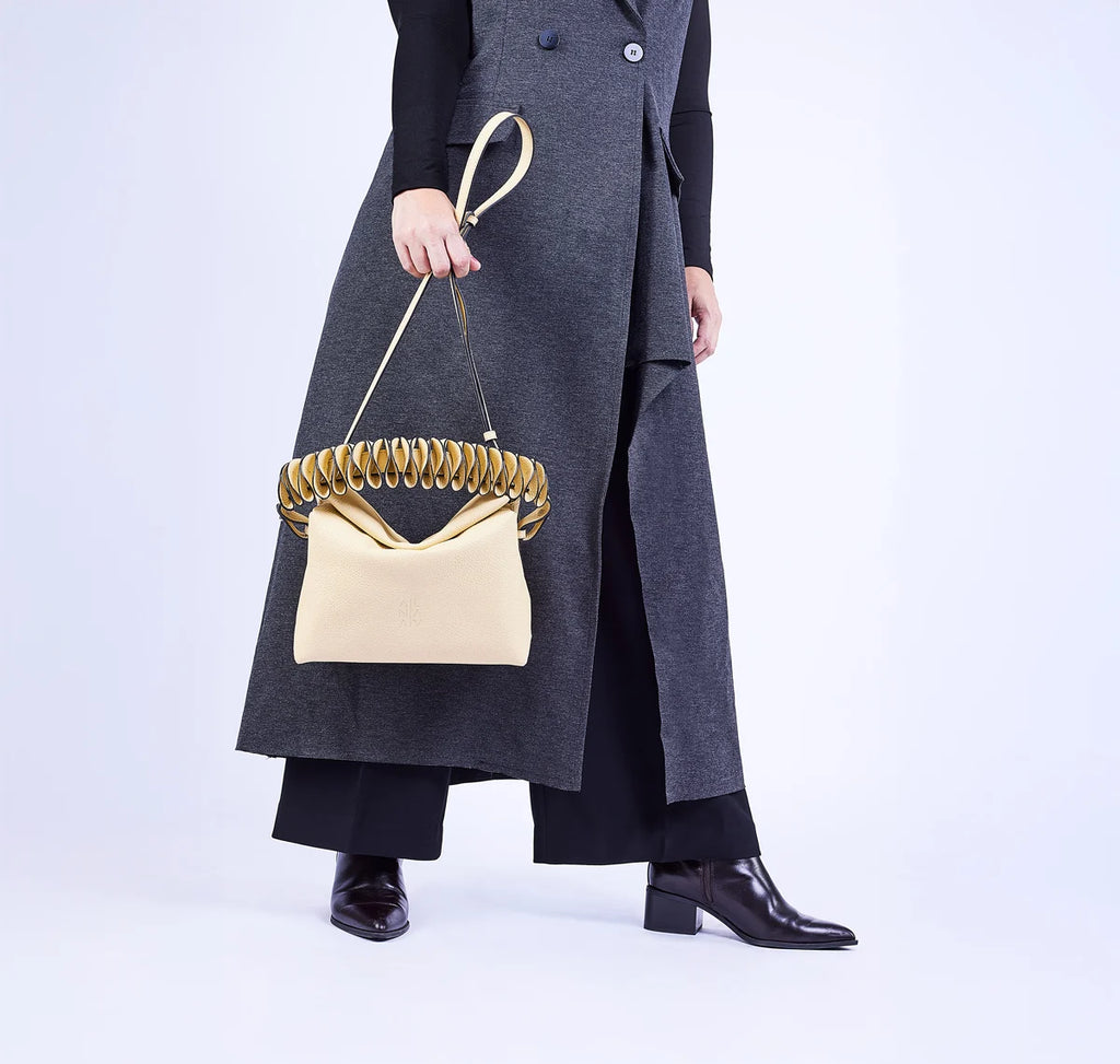 Person wearing a long dark coat holding a yellow handbag with an architectural strap on a white background