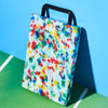 Colorful splatter-patterned cutting board with a black handle on a green and blue background
