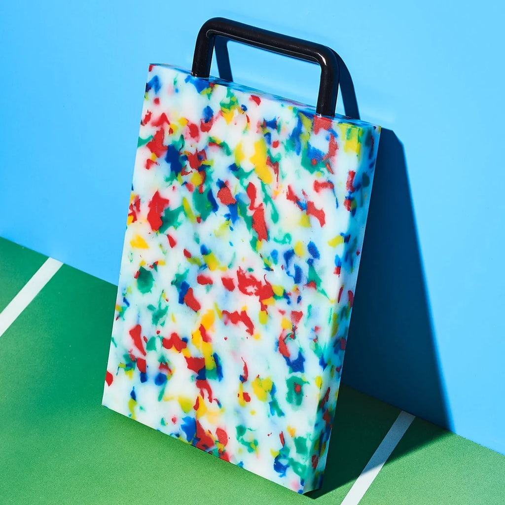 Colorful splatter-patterned cutting board with a black handle on a green and blue background