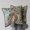 Person holding two decorative pillows with intricate patterns against a plain background