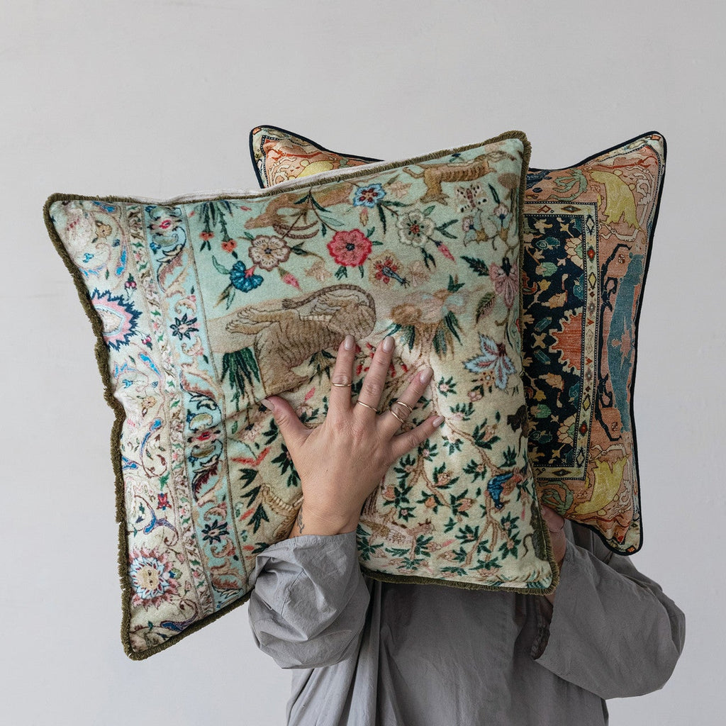 Person holding two decorative pillows with intricate patterns against a plain background